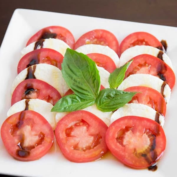 Caprese salad with sliced tomatoes, mozzarella, balsamic glaze, and fresh basil on a white plate.