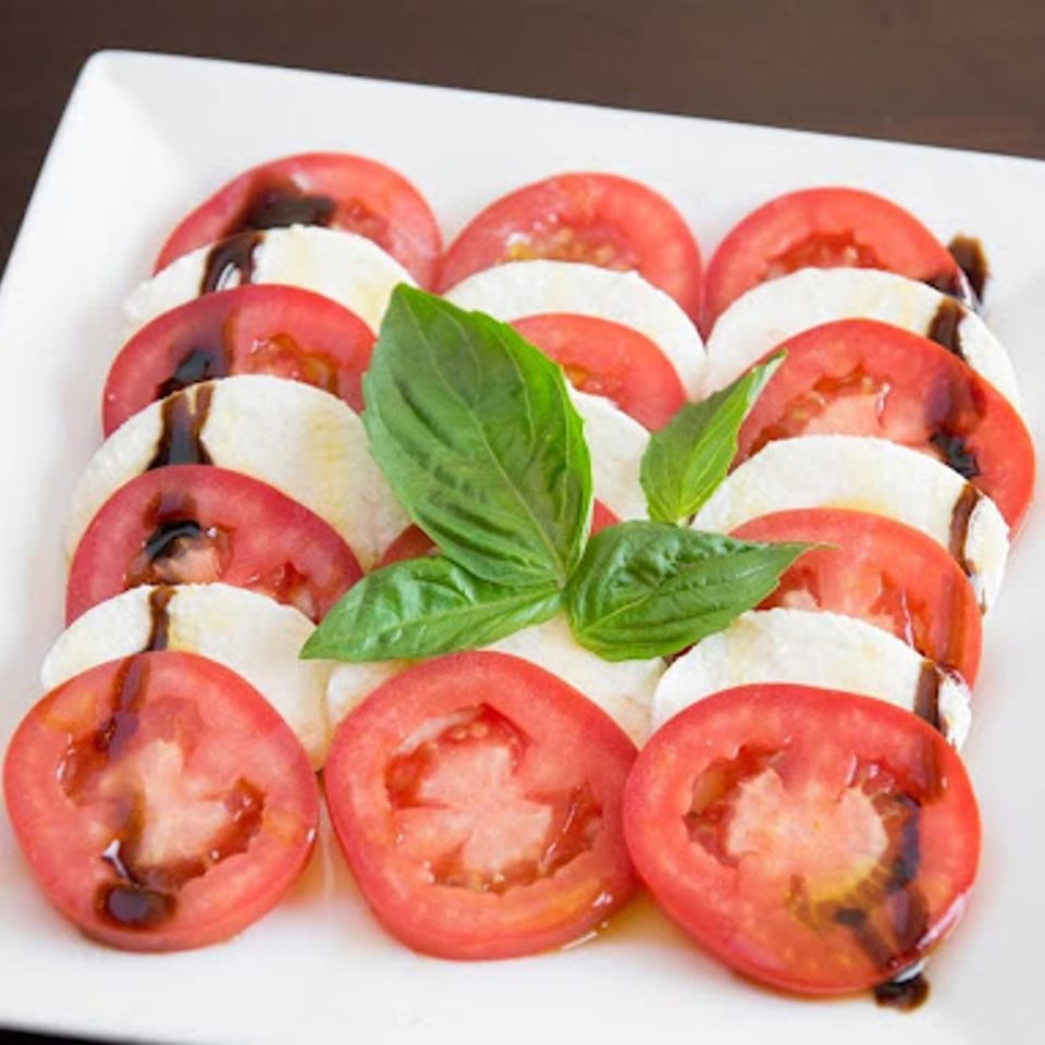 Caprese salad with sliced tomatoes, mozzarella, balsamic glaze, and fresh basil on a white plate.