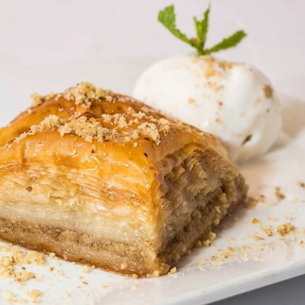 A piece of baklava topped with nuts and honey, served with a scoop of vanilla ice cream and mint.